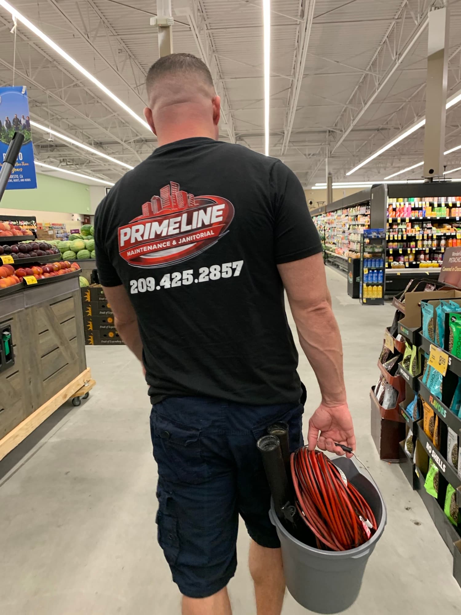Primeline Maintenance & Janitorial crew member carrying cleaning equipment through a grocery store aisle